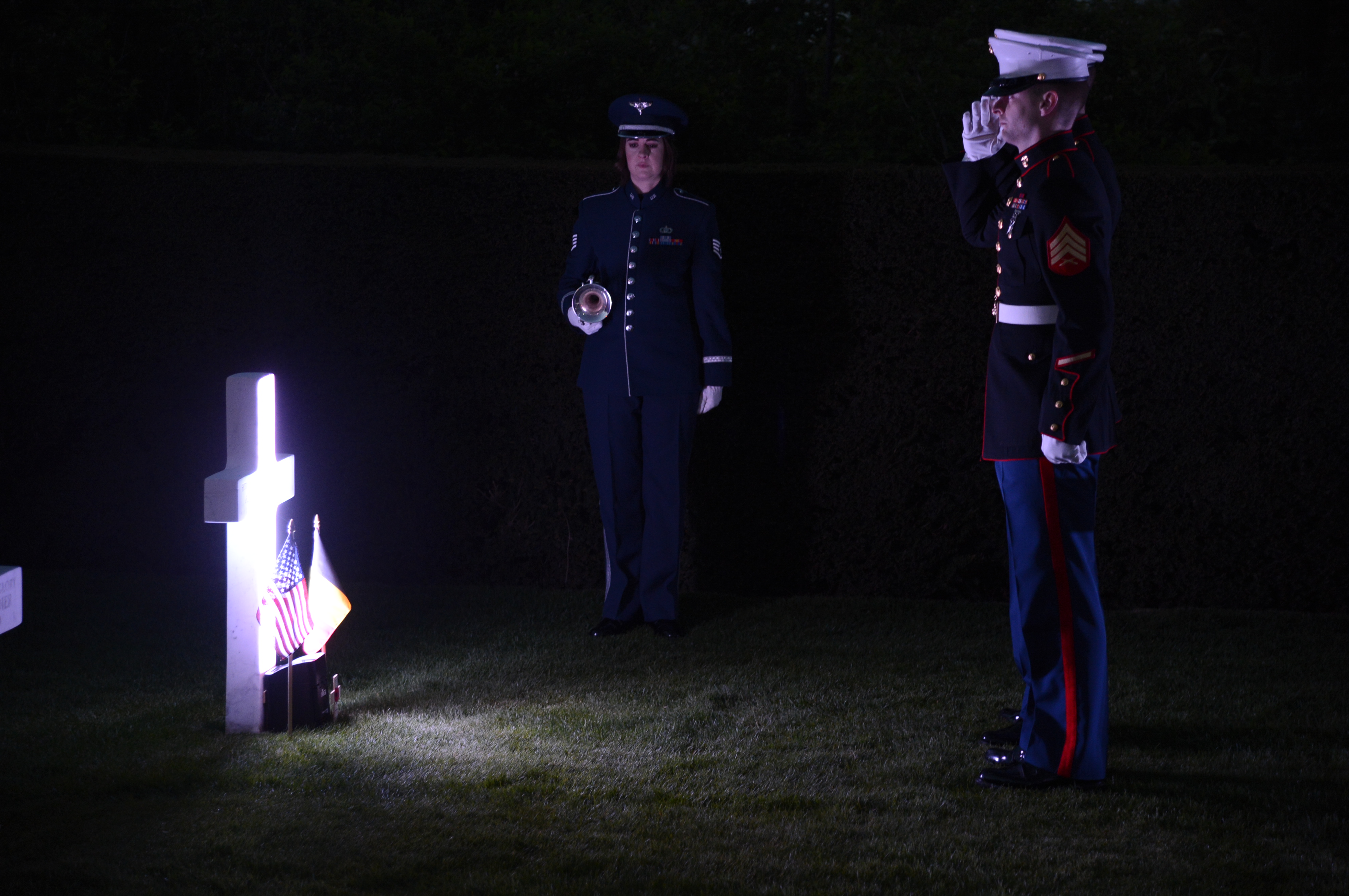 Light shines on a single headstones as two Marines salute. 