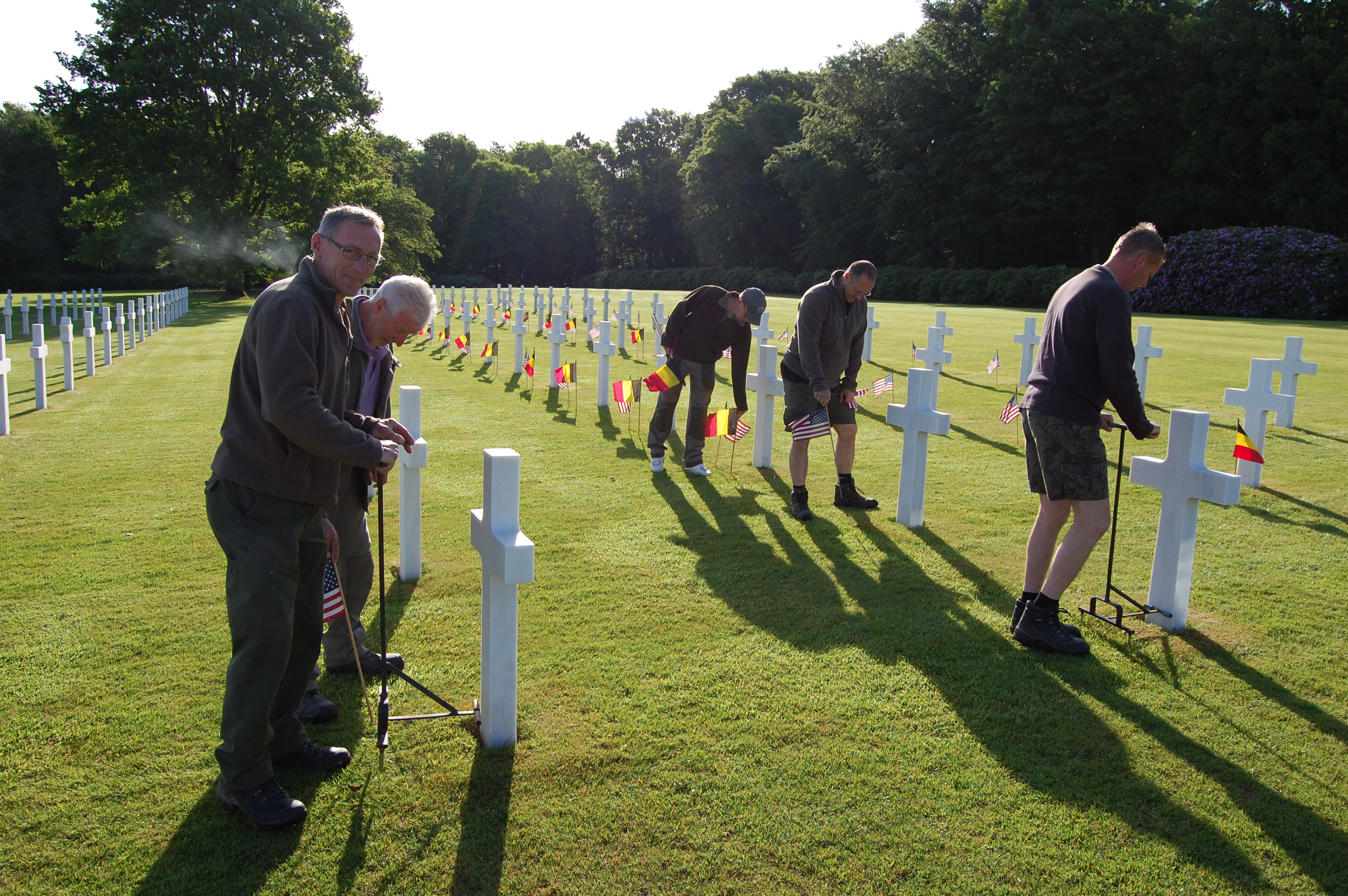 Men place American and Belgian flags in front of every headstone. 