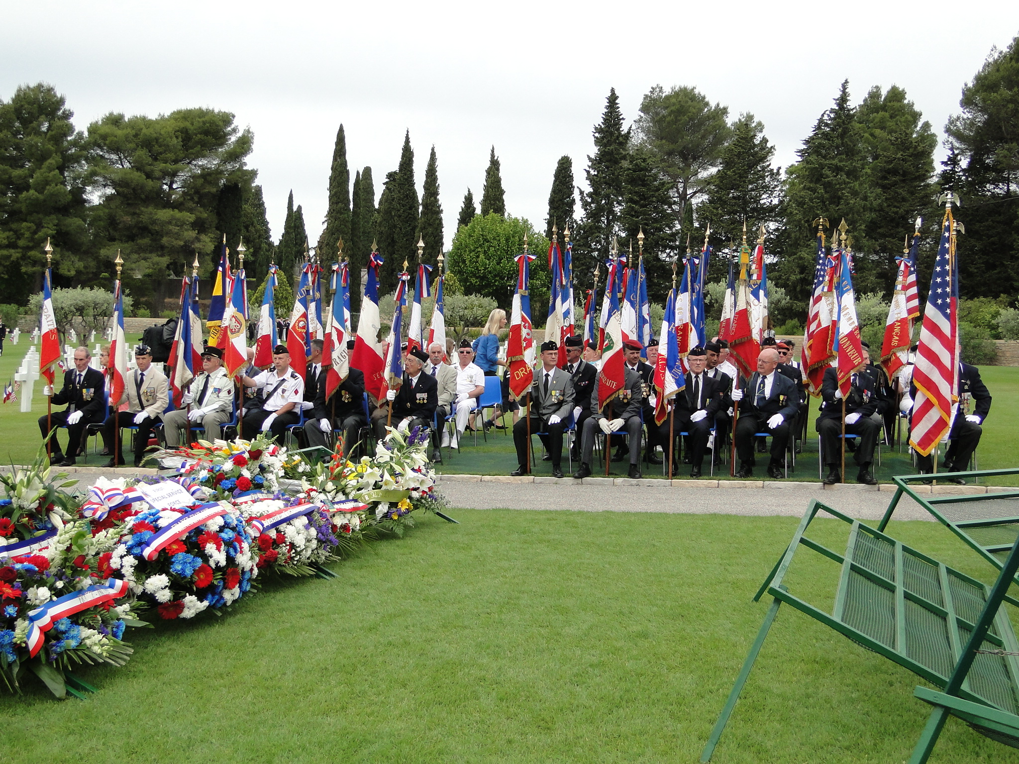 Flag bearers sit in chairs near the floral wreath stands. 