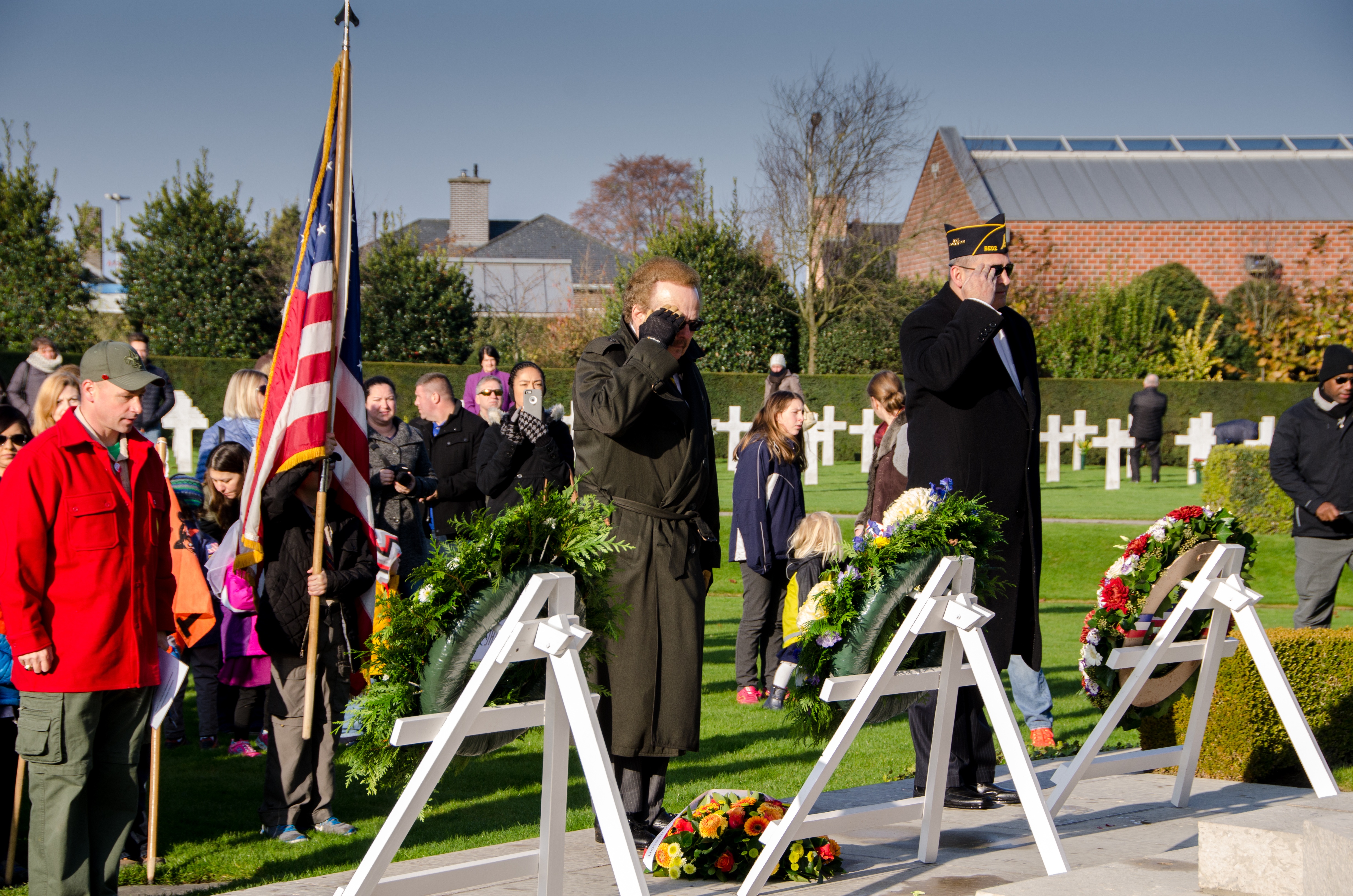 Two men stand and salute after laying floral wreaths.