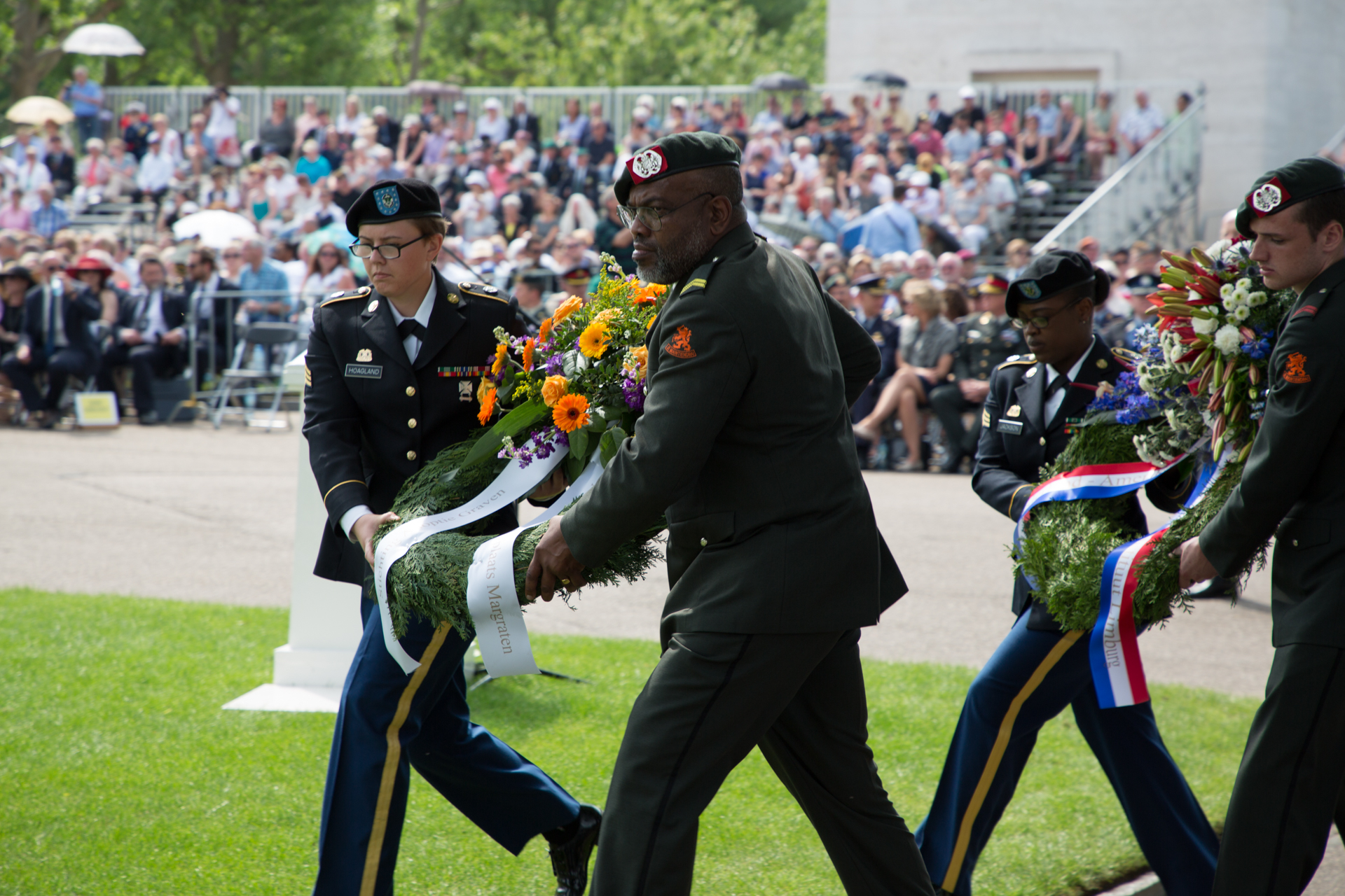 Men and women in uniform carry floral wreaths. 