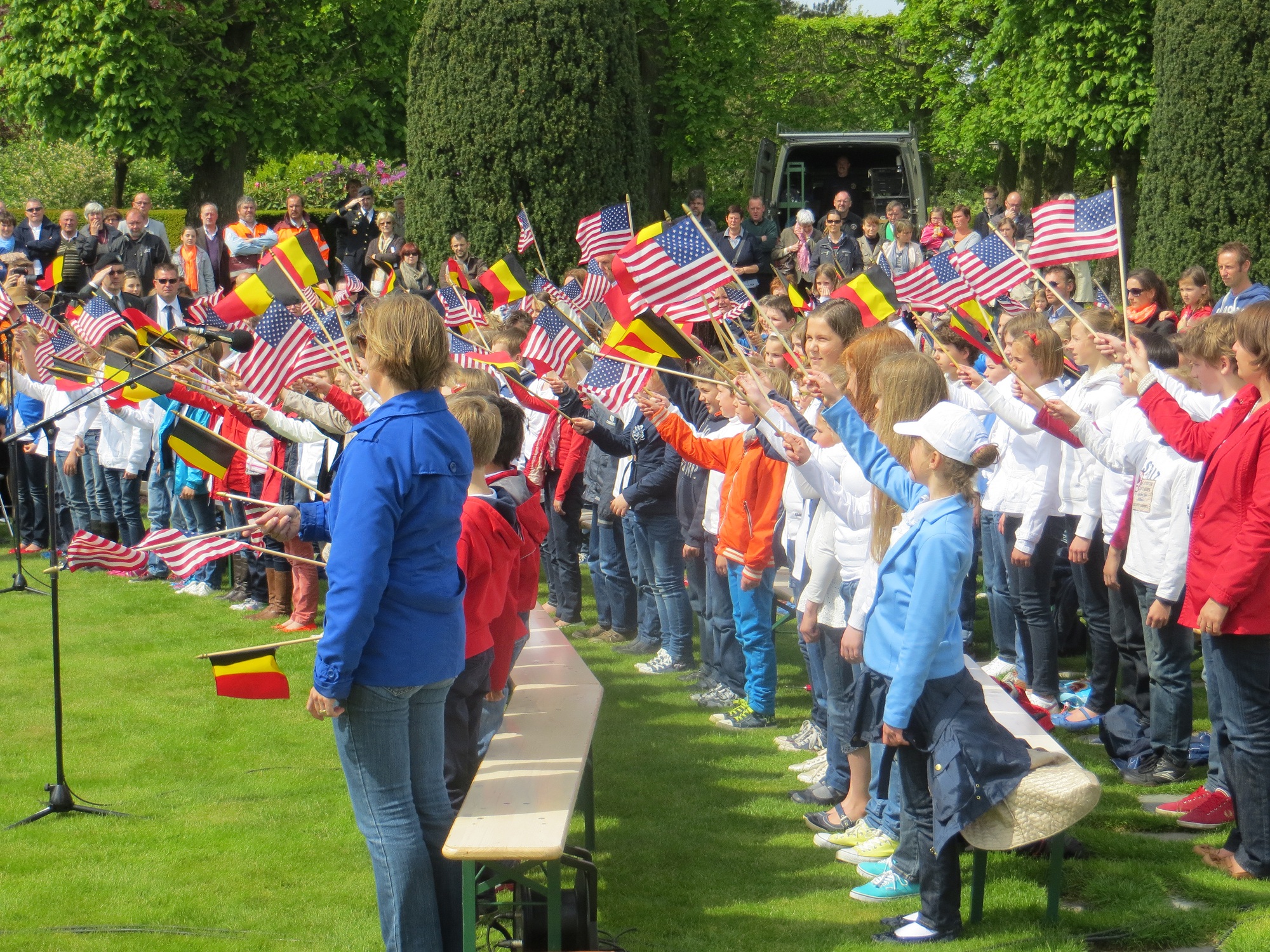 Rows of school children wave American and Belgian flags. 
