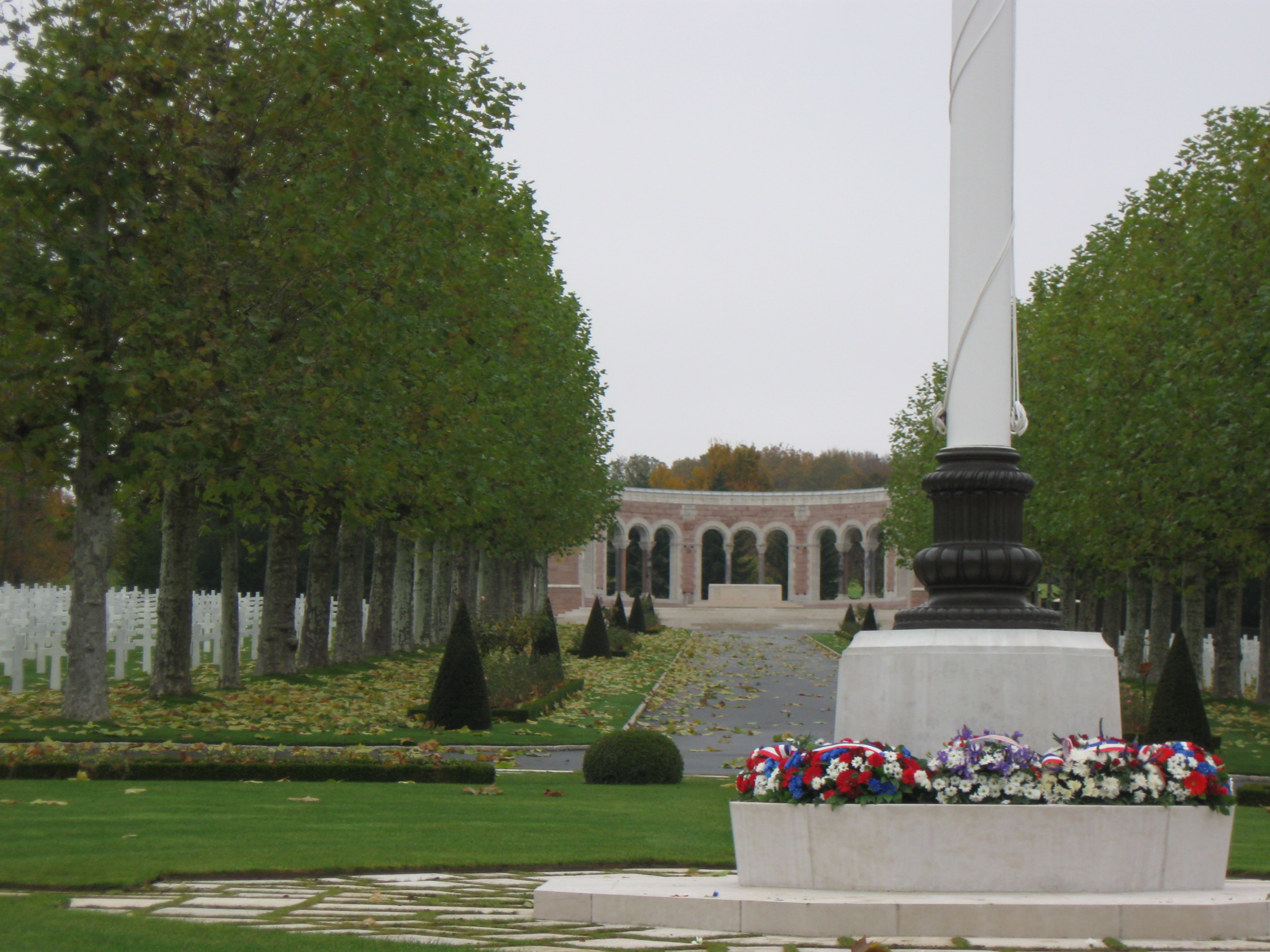 Wreaths lie at the base of a flag pole, with headstones and the chapel in the background, at Oise-Aisne American Cemetery for the 2012 Veterans Day ceremony.