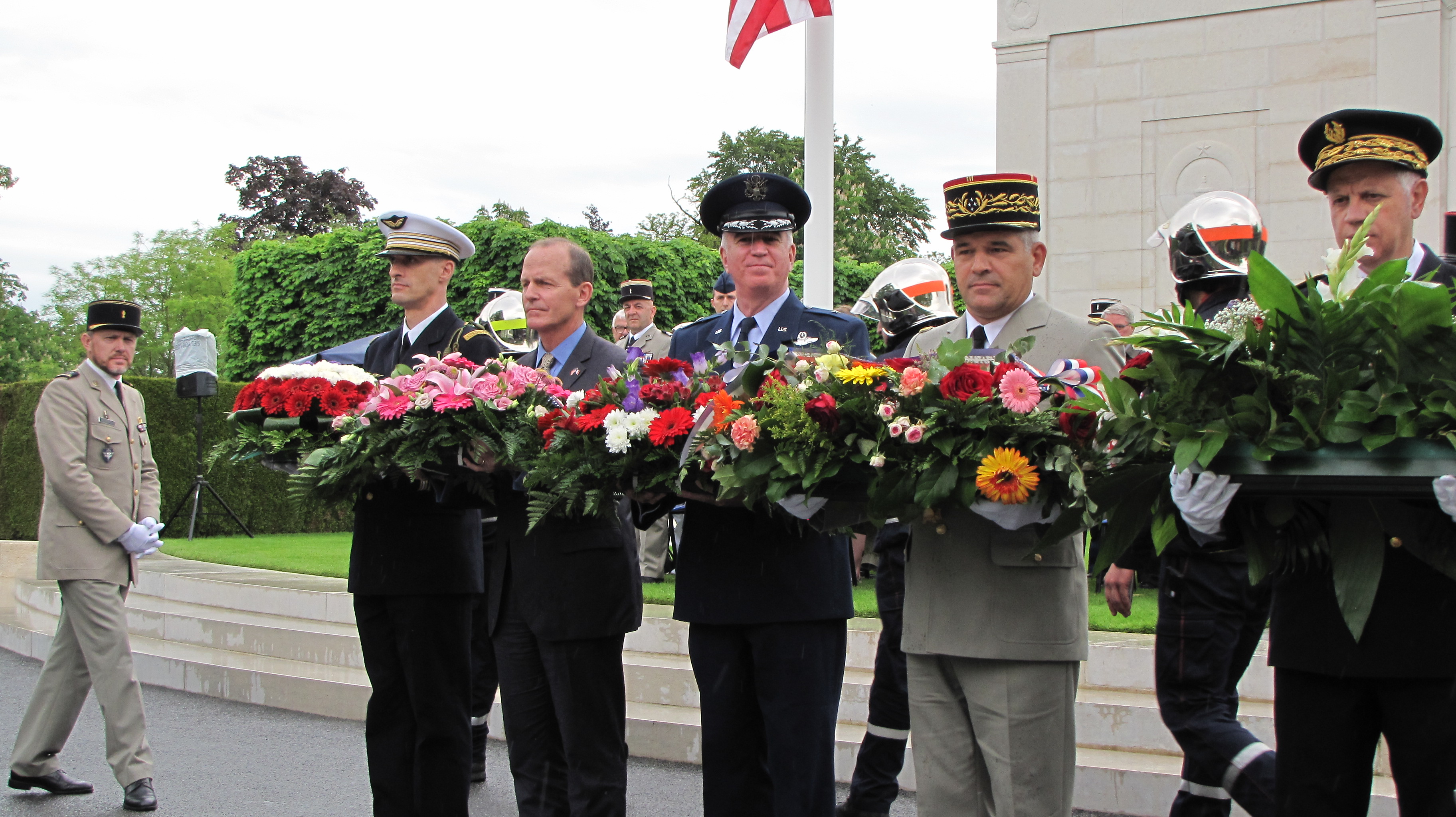 Men hold floral wreaths in preparation for wreath laying. 