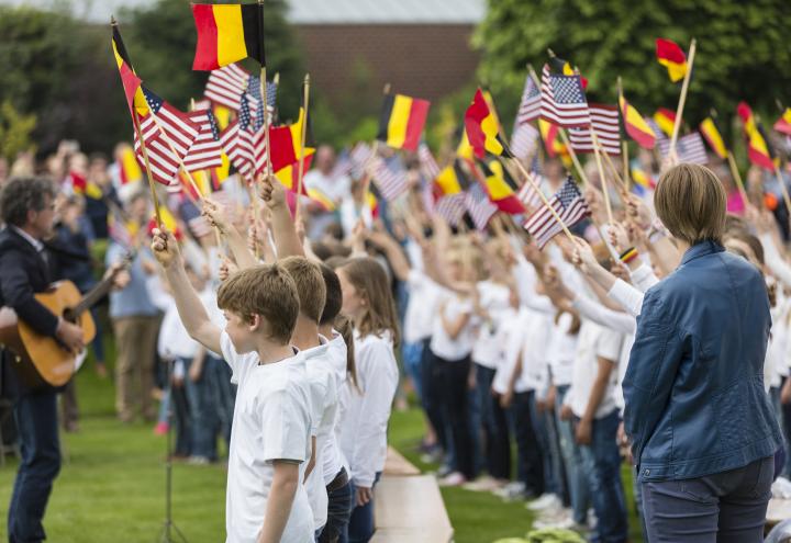 Children wave American and Belgian flags as they sing. 