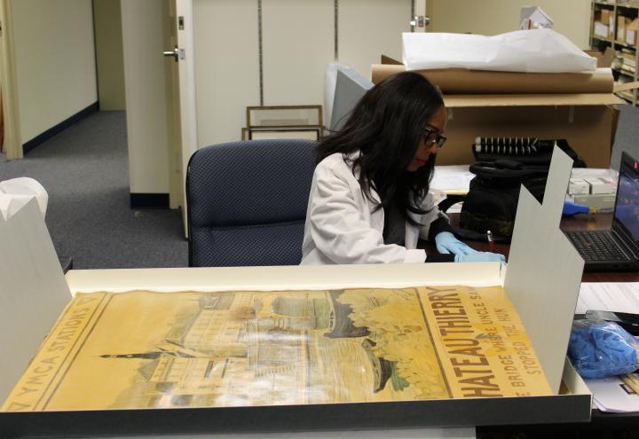 Thomas, in a white coat and gloves, works to process the historic poster. 