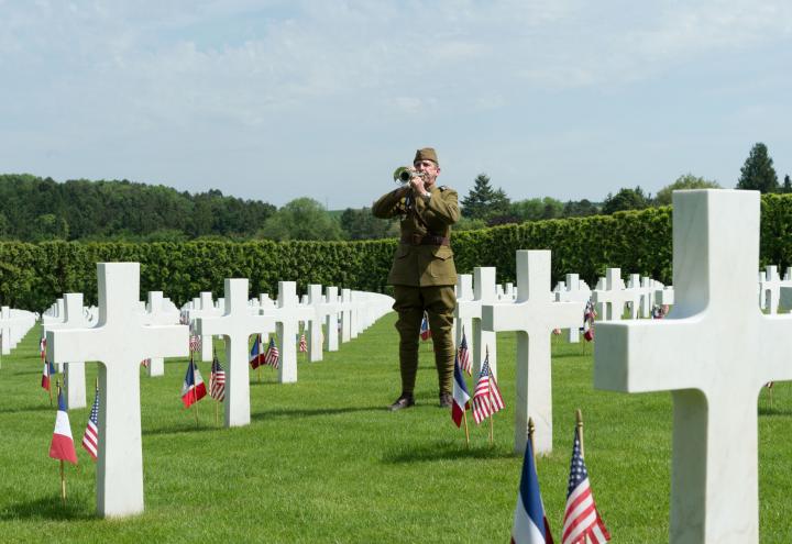 A man in a doughboy uniform plays the bugle amidst the headstones.