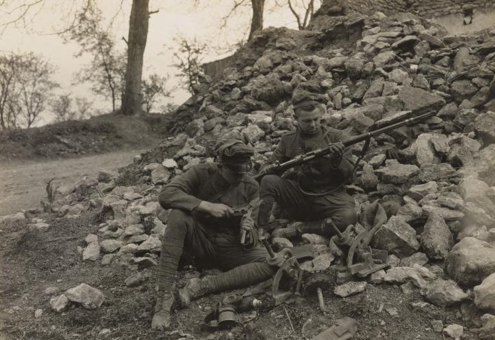 Historic photo shows soldiers sitting on rubble examining items.