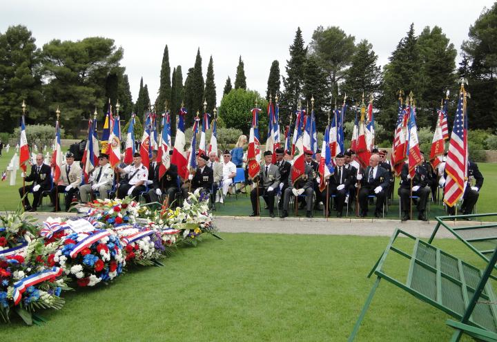 Flag bearers sit in chairs near the floral wreath stands. 