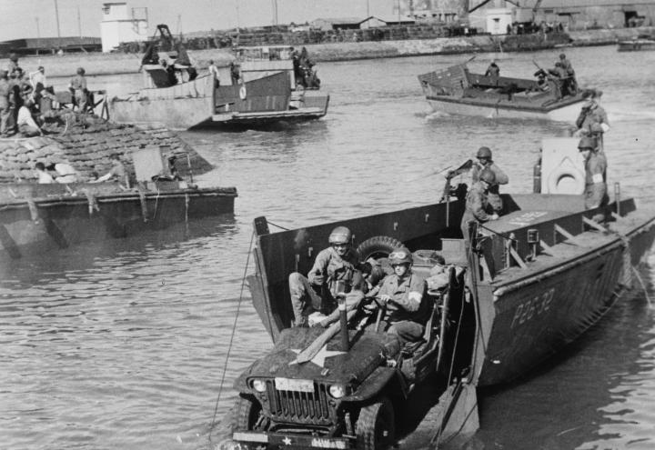 Historic photo showing jeep coming off landing craft. 
