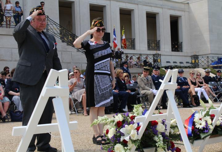 A man and woman salute after laying a wreath.