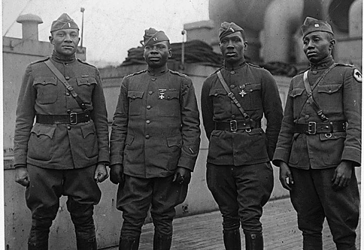 Historic photos shows four men in uniform aboard a ship. 