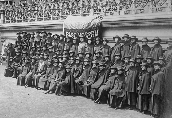 Historic photo showing rows of women in long dresses, capes and hats.