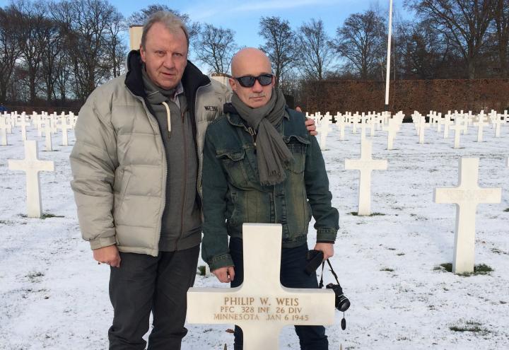 Two men stand behind the headstone, and snow covers the ground.