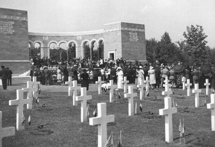 Historic photo shows headstones with flags and a crowd gathered in the memorial area. 