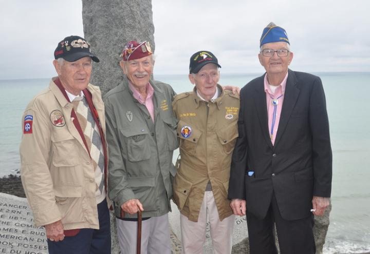 Four World War II veterans stand in front of the Ranger Monument at Pointe du Hoc.