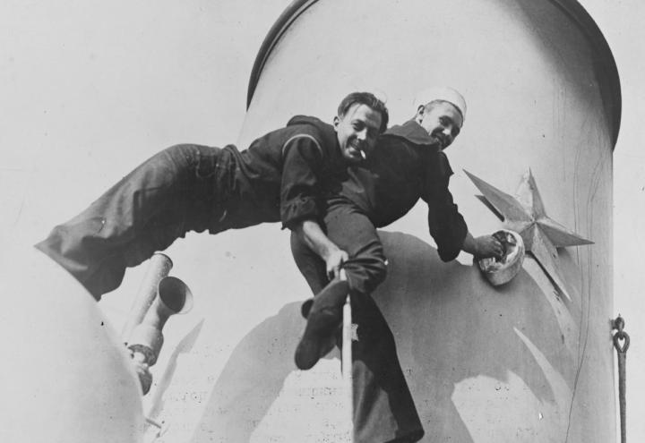 Historic photo shows two men smiling while working on the smokestack. 