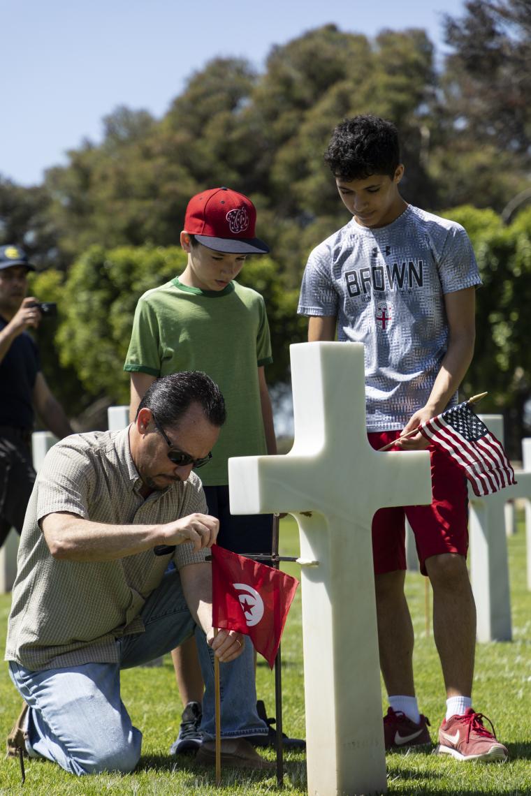 Ambassador Rubinstein kneels down while placing flags at a headstone. 