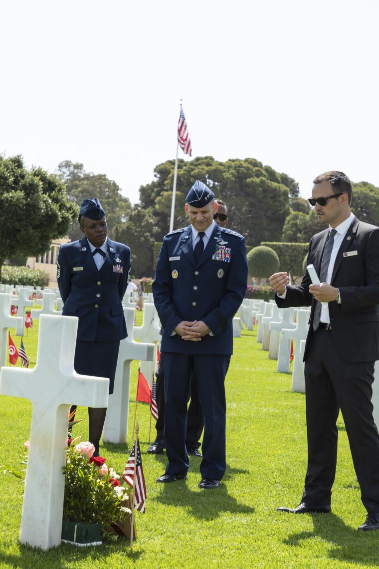 Men and women in uniform look at a headstone while the assistant superintendent talks. 