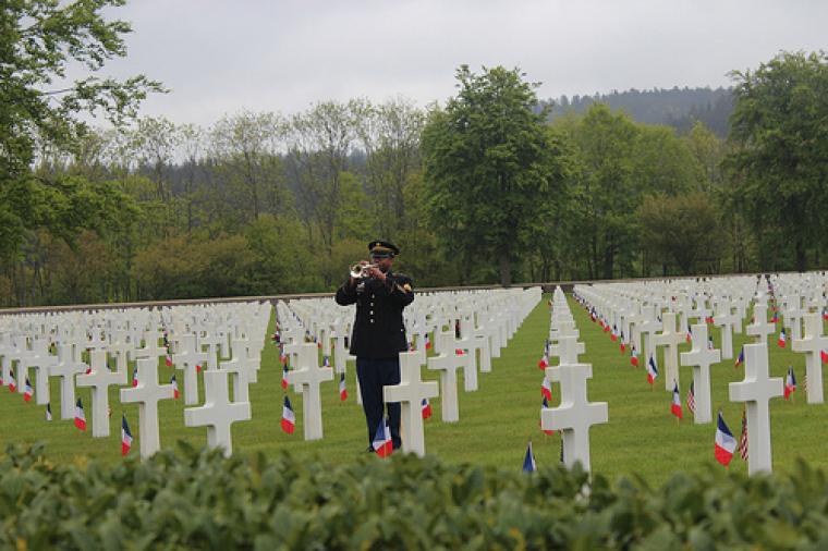 A bugler stands amongst the headstones. Each headstone has an American and French flag. 