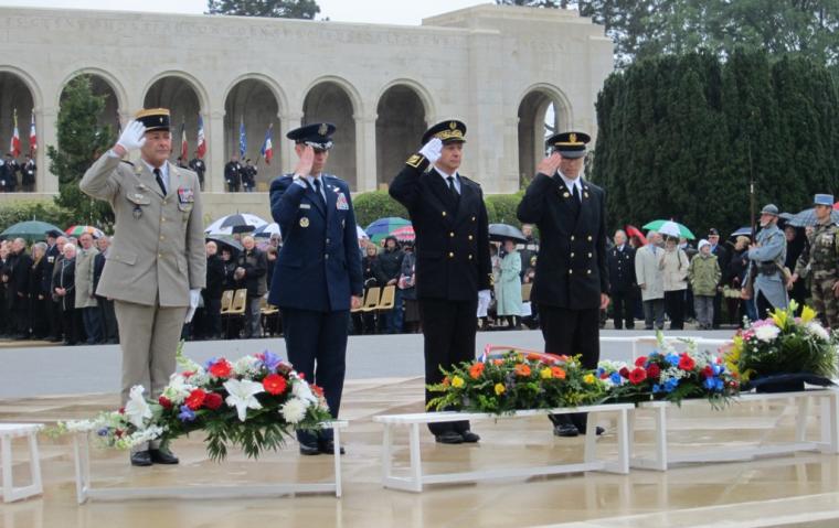Men in uniform salute after laying wreaths. 