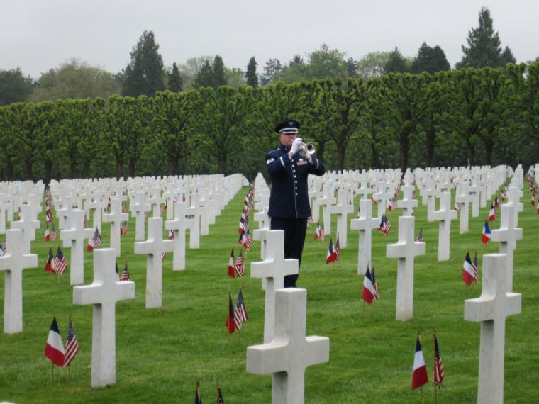 A bugler stands amongst the headstones. Each headstone has an American and French flag.