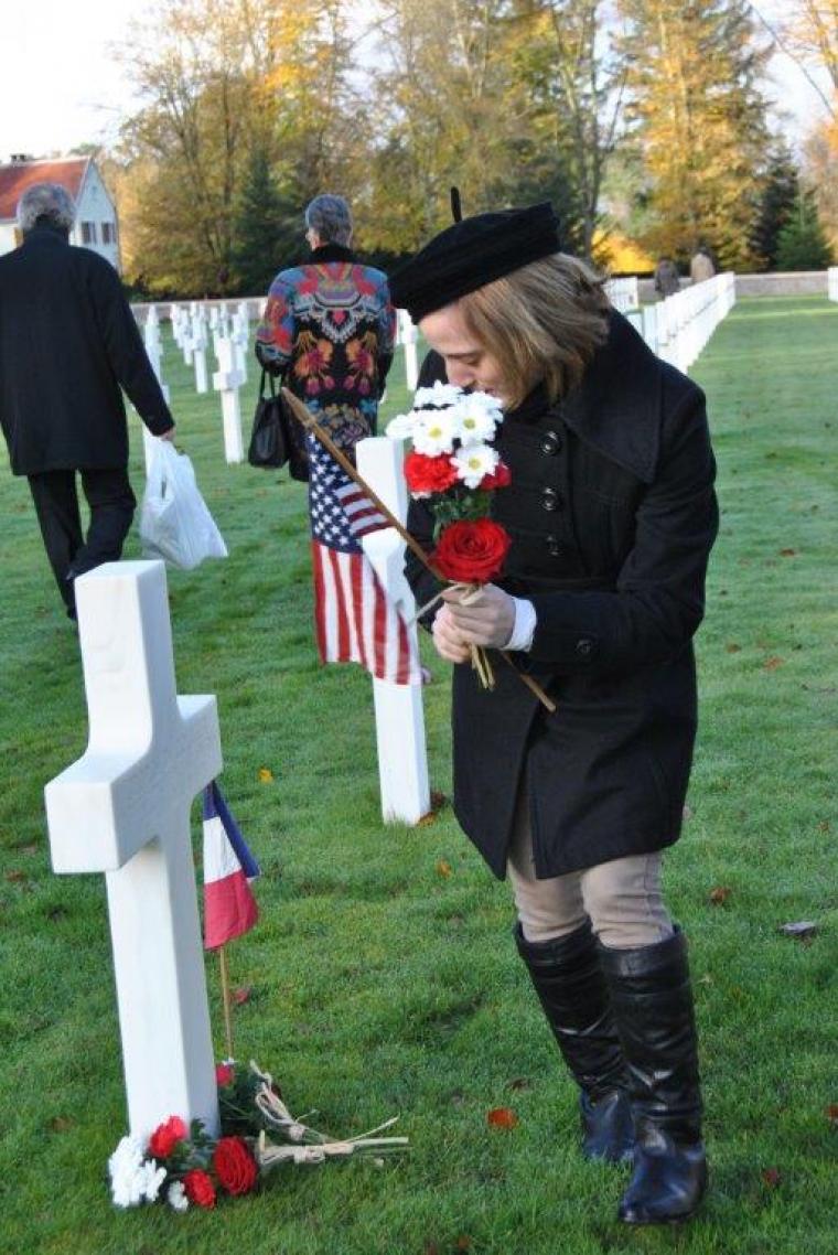 A woman lays flowers at the base of a headstone. 
