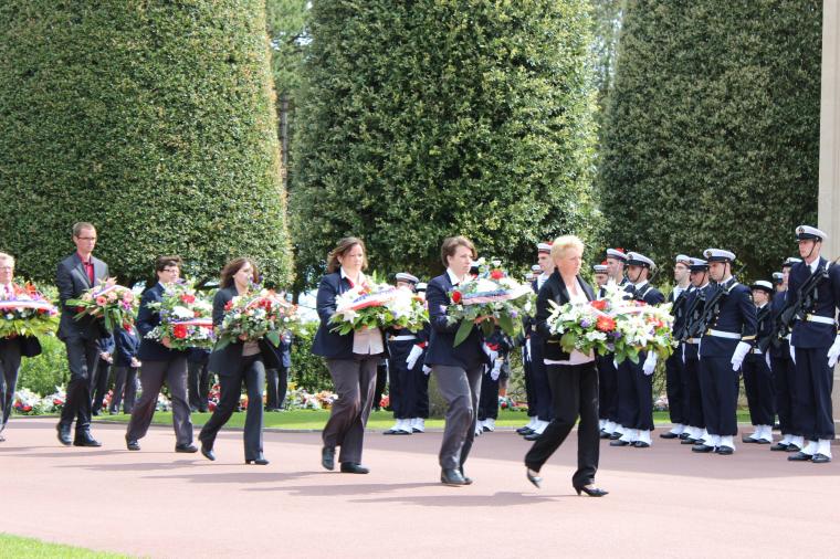 Staff walk in a line carrying the floral wreaths. 