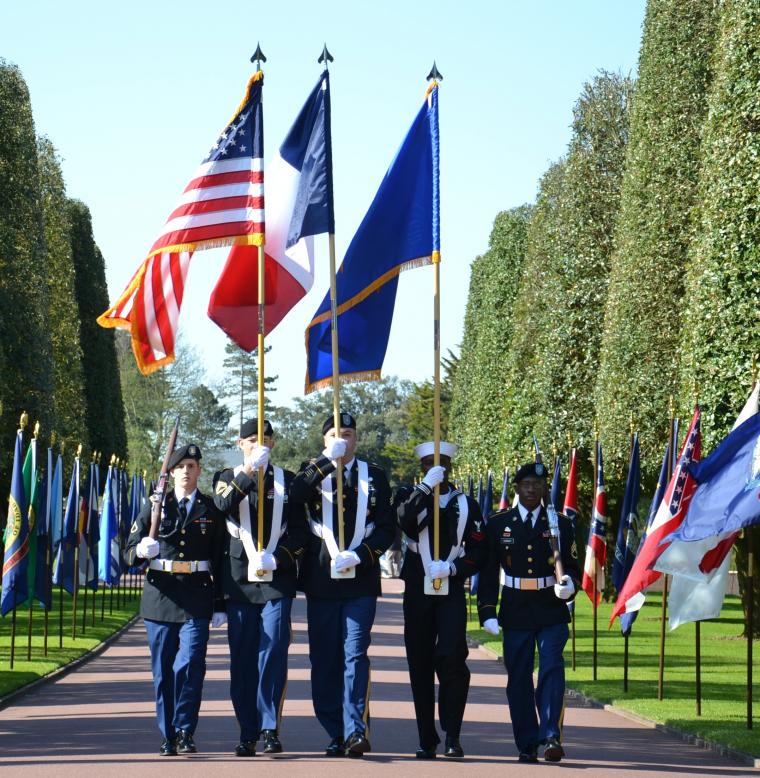 A U.S. Color Guard marches into the cemetery down a flag-lined path. 