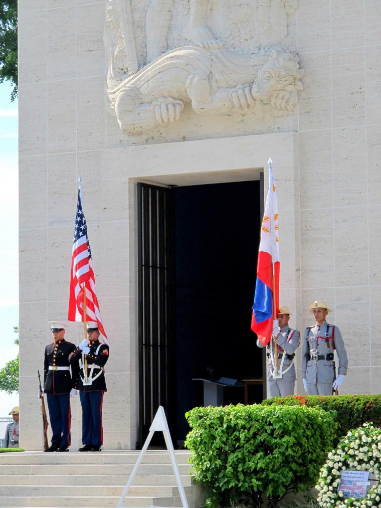 Members of military stand outside chapel with country flags. 