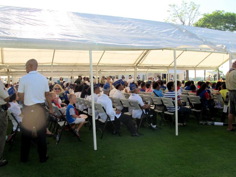 Attendees sit under a tent. 