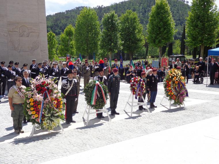 Large floral wreaths sit on stands next to the participants that laid the wreaths. 