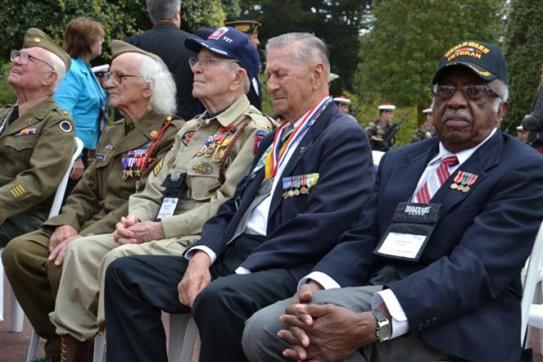World War II veterans sit in chairs during ceremony. 