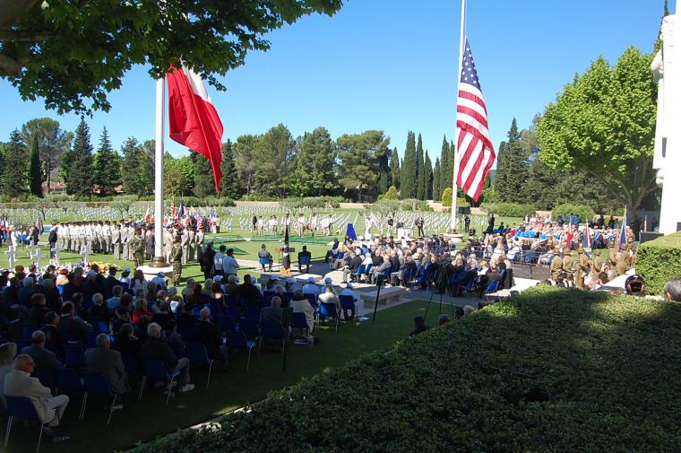 A large crowd attends the ceremony and large French and American flags are at half mast. 