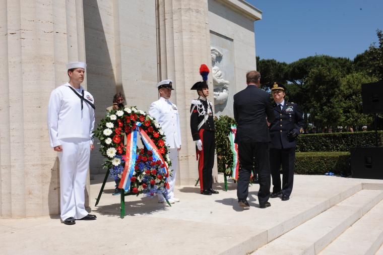 Members of the military stand next to floral wreaths. 