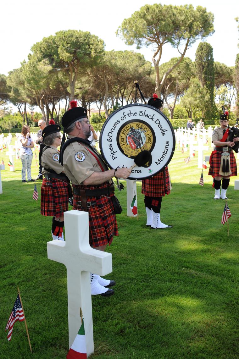 Bagpipers and drummers stand amongst the headstones, ready to play. 