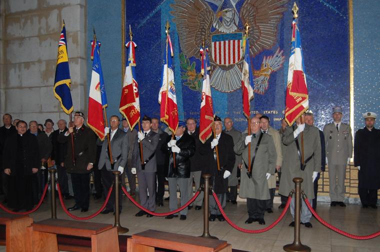 Participants with flags gather in front of a mosaic wall in the chapel at Rhone American Cemetery for the 2012 Veterans Day ceremony.