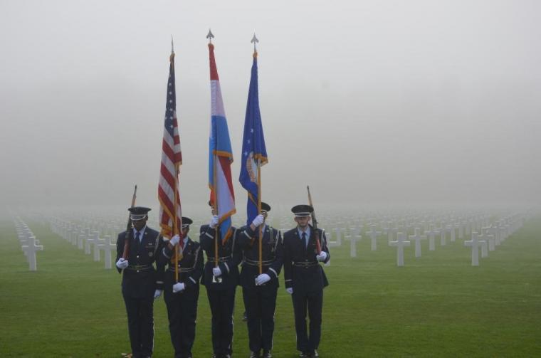 A color guard stands with flags in front of headstones. 
