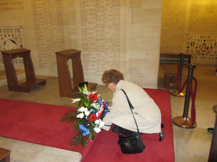 A woman kneels to the ground and lays a wreath in the chapel at Aisne-Marne American Cemetery.