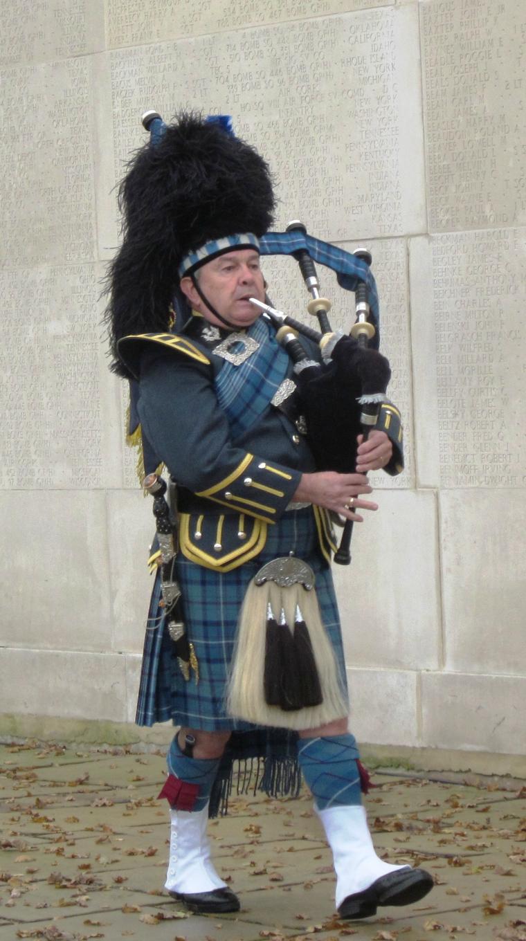 A bagpiper stands in front of the Walls of the Missing at Cambridge American Cemetery. 