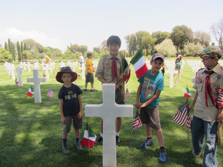 Boy scouts stand with flags near a headstone. 