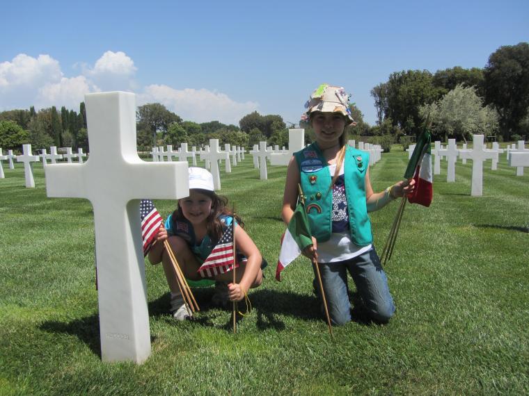 Girl scouts with flags near a headstone. 