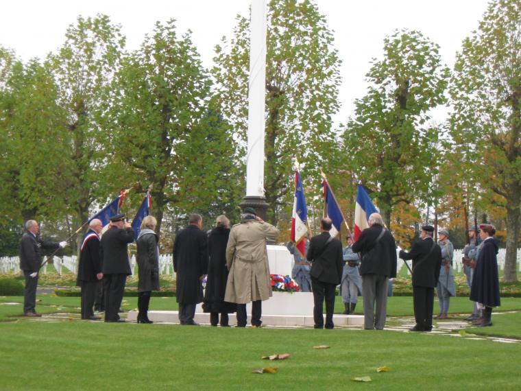 Participants stand around a flag pole, where wreaths lay at the base, as part of the 2012 Veterans Day ceremony at Oise-Aisne American Cemetery.