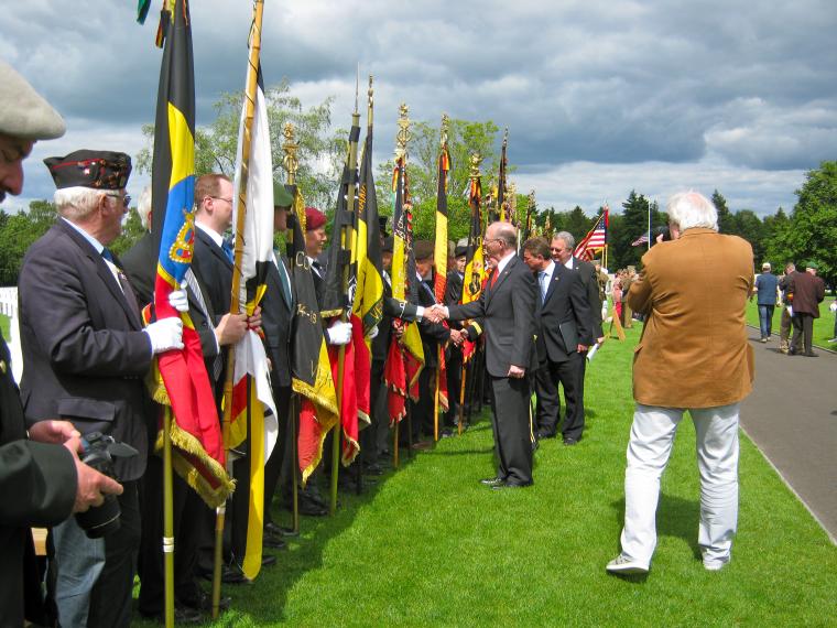 Flag bearers stand in a line, and are greeted by a group of men. 