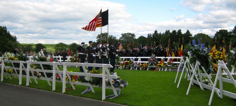 Floral wreaths on stands with a color guard in the background. 