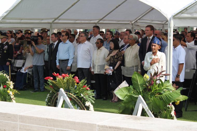 Attendees stand under a tent during the ceremony. 