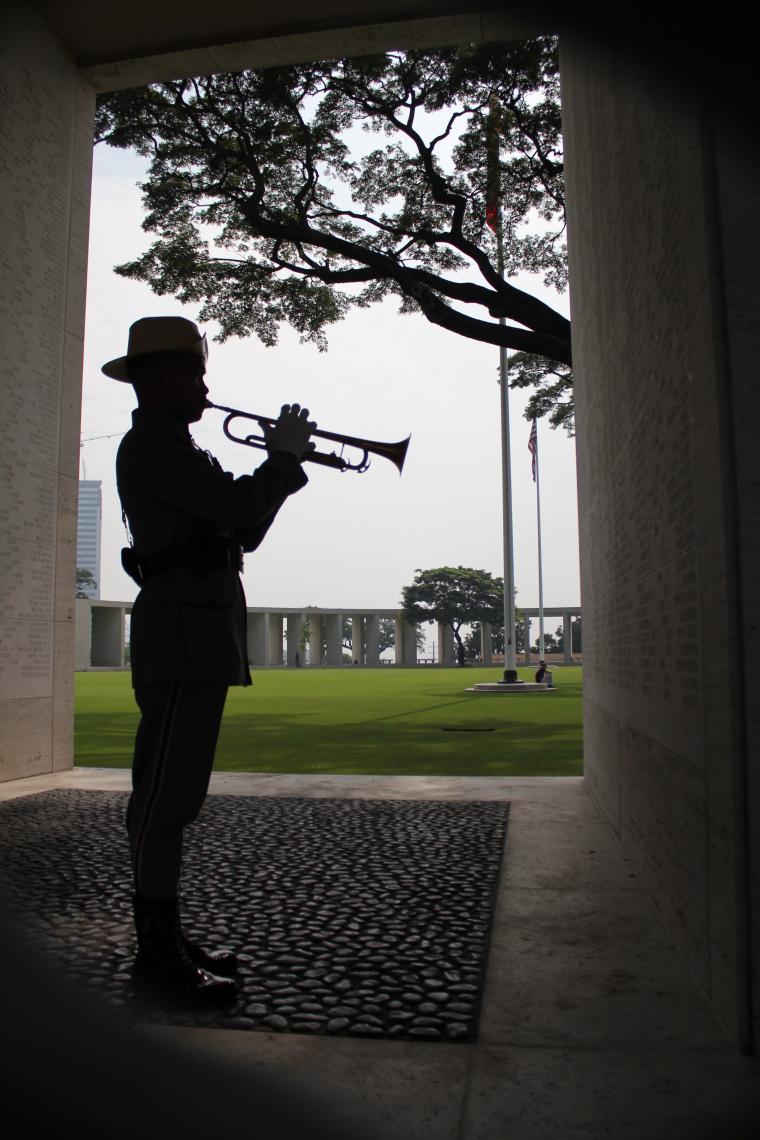 A man stands next to the Wall of the Missing playing the bugle. 