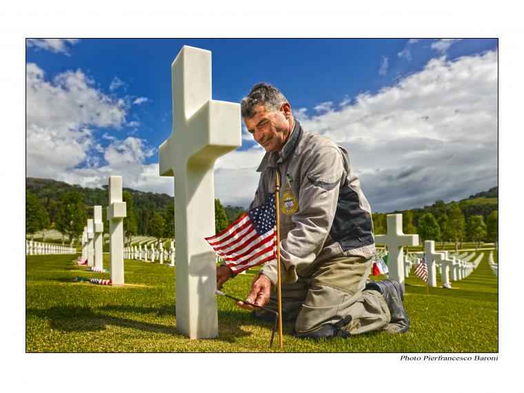 Man places flags in front of headstones. 