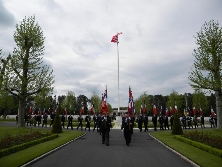 French flag bearers walk in a line as they exit the cemetery. 