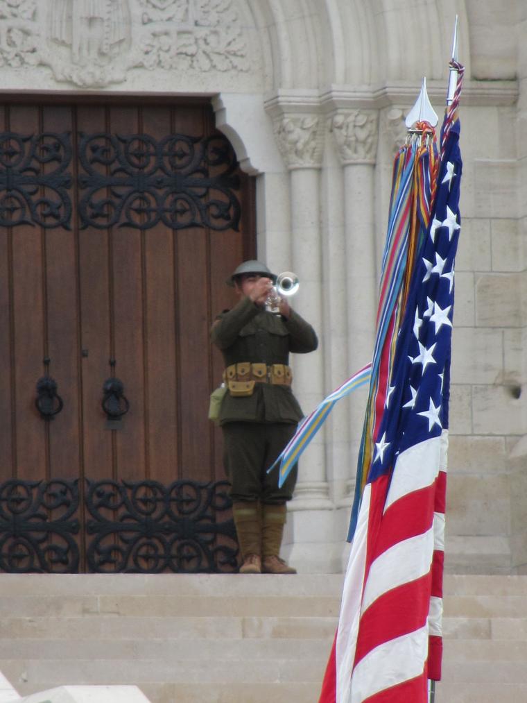 A man in a WWI era uniform plays the bugle on the steps of the chapel.